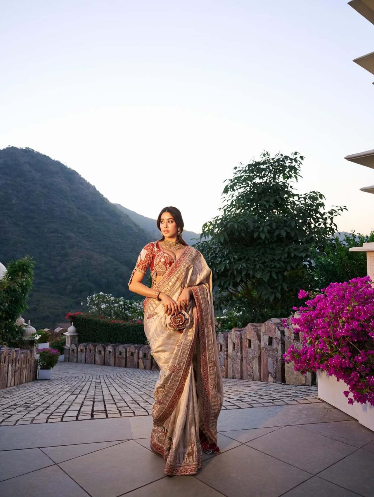 This ivory silk saree with intricate borders is pure festive royalty. Styled with heritage jewellery and a statement potli, it balances tradition and sophistication beautifully. Ideal for wedding pujas or family functions with a grand backdrop